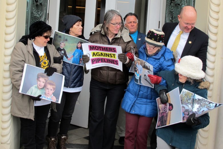 Protestors fighting new fossil fuel pipelines huddle together with posters.