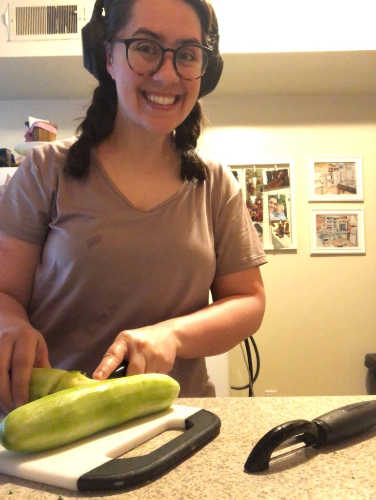 author Lauren Landis smiling and chopping a cucumber with her headphones; photos in the background on the wall and vegetable peeler in foreground