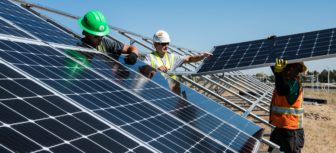 construction workers with hard hats position solar panels on metal frames outdoors